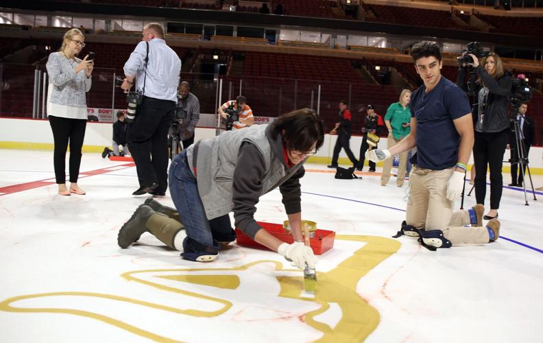 Blackhawks defenseman Trevor van Riemsdyk, kneeling to the right kneeling, takes part in the traditional painting of the  team's logo at center ice.