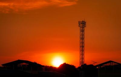 Telecommunication tower with red sunset sky and clouds. Radio and satellite pole. Communication technology. Telecommunication industry. Mobile or telecom 4g network. Silhouette rural house and forest.