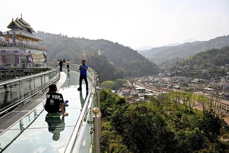 Visitors walk on a skybridge overlooking Myanmar's border town of Tachileik (R) at Wat Phra That Doi Wao Buddhist temple in Mae Sai in the northern Thai province of Chiang Rai on March 17, 2026.