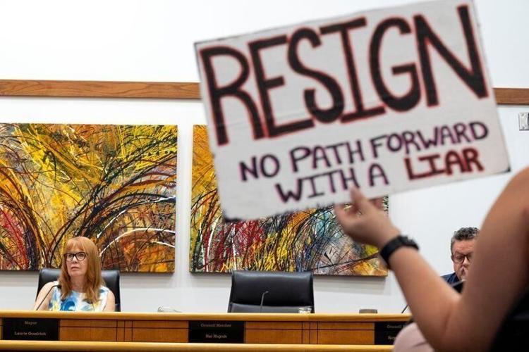 Mayor Laurie Goodrich takes her place at the dias as a constituent holds a sign calling for her resignation Aug. 25, 2026 during a Coralville City Council meeting in Coralville, Iowa.