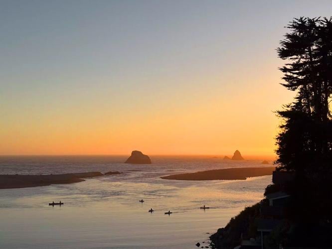 Kayakers paddle through sunset on the Russian River estuary, which looks out at the sea and sea stacks near Jenner.