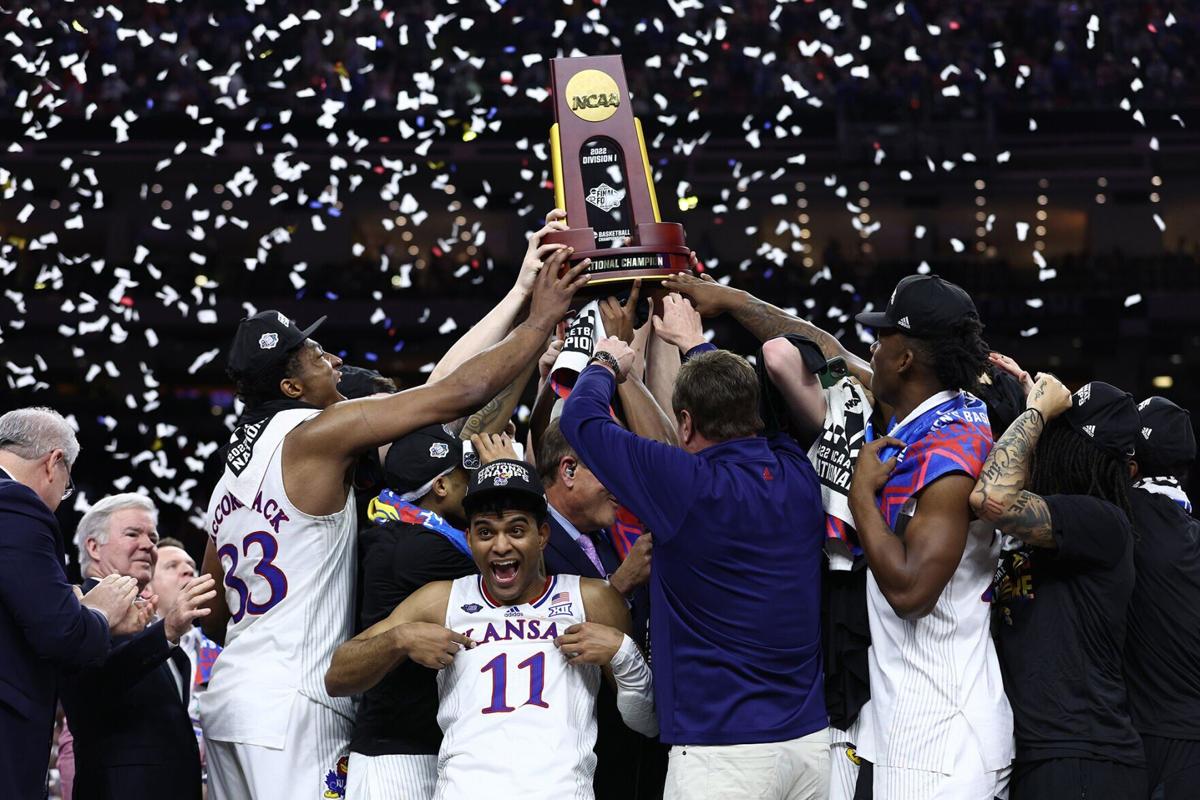 Remy Martin of the Kansas Jayhawks reacts as Kansas Jayhawks players and coaches hold up the trophy after defeating the North Carolina Tar Heels 72-69 during the 2022 NCAA Men's Basketball Tournament National Championship at Caesars Superdome on April 0...