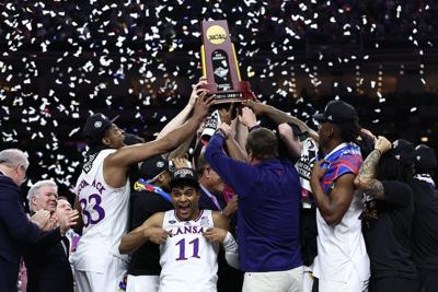 Remy Martin of the Kansas Jayhawks reacts as Kansas Jayhawks players and coaches hold up the trophy after defeating the North Carolina Tar Heels 72-69 during the 2022 NCAA Men's Basketball Tournament National Championship at Caesars Superdome on April 0...