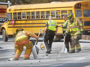 Stowe police and firefighters clean up debris and begin taking measurements in investigating a collision between a school bus and a car on Mountain Road on Tuesday.