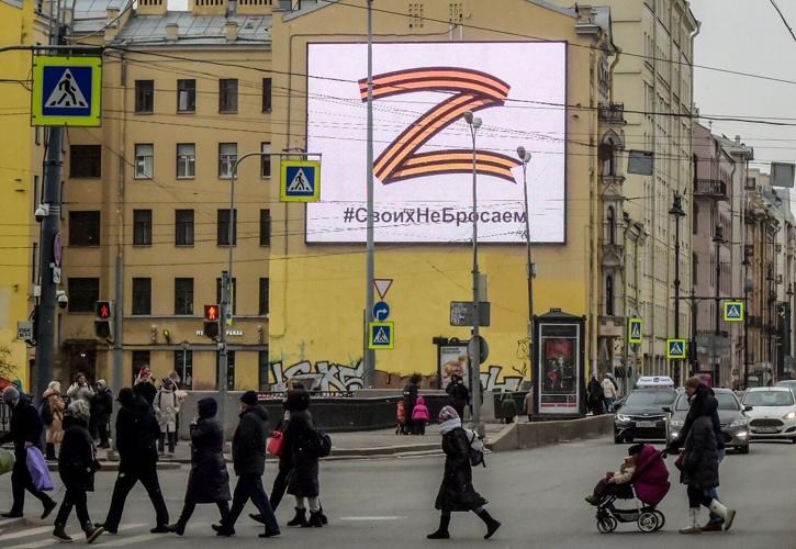 Pedestrians cross a street in front of a billboard displaying the symbol "Z" in the colors of the ribbon of Saint George and a slogan reading: "We don't give up on our people," in support of the Russian armed forces, in Saint Petersburg, on March 7, 2022.