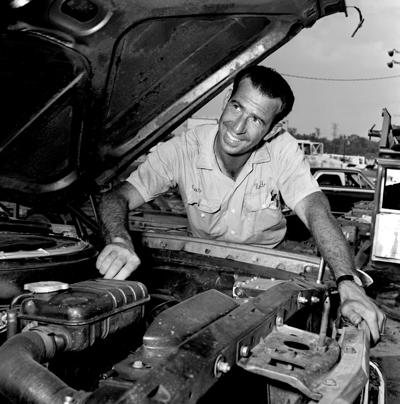 Driver Ned Jarrett takes no chances on anything going wrong under the hood of his 64 Ford as he inspects it with as much care as his favorite service station attendant. Jarrett died on June 4, 2026 at the age of 93.