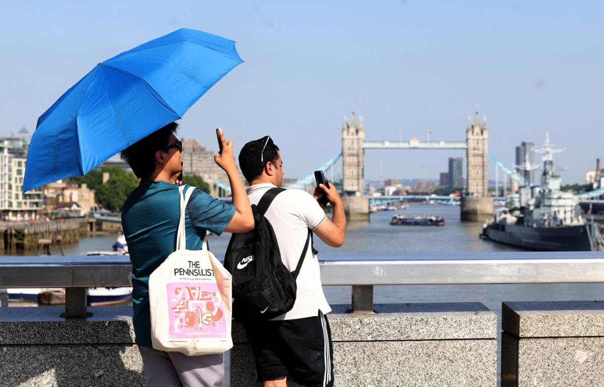 Tourists shelter from the sun beneath a parasol umbrella whilst taking photographs over the River Thames, during a heatwave, in central London on June 24, 2026. The UK recorded its hottest ever June temperature on Wednesday with the mercury rising to 35...