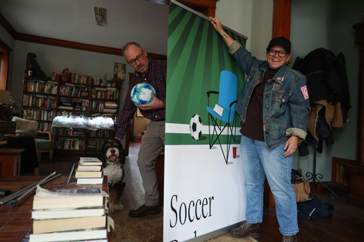 Cristie Bosch unfurls a book cover promotional poster for "Soccer Dad," written by her husband, David Murray, left, at their home Thursday, April 9, 2026, in Chicago.