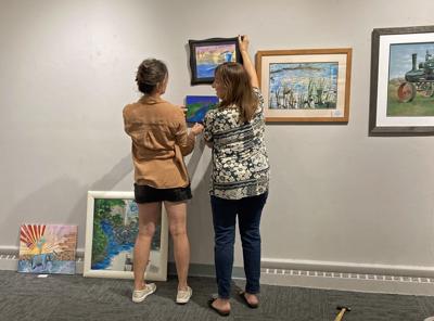 Portage Center for the Arts visual arts committee members, Lorisa Harvey, left, and Laura Johnson, hang the Collaborative Community Art Exhibit on Tuesday for the opening reception Friday.