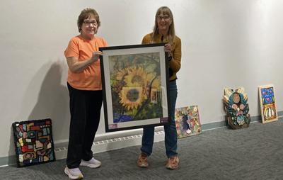 Portage Center for the Arts Visual Arts Committee members Peg Napralla, left, and Liz Gregory, hang the art for the show on Tuesday; fresh floral arrangements and poetry will accompany the artwork. Exhibit opens Friday and runs through June 26.