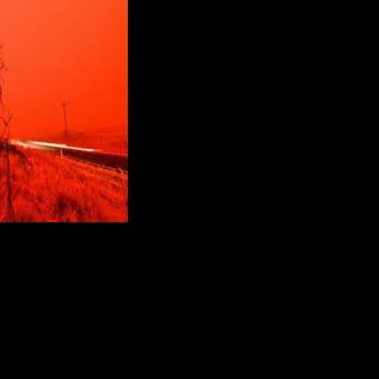 A long exposure picture shows a car commuting on a road as the sky turns red from smoke of the Snowy Valley bushfire on the outskirts of Cooma on January 4, 2020